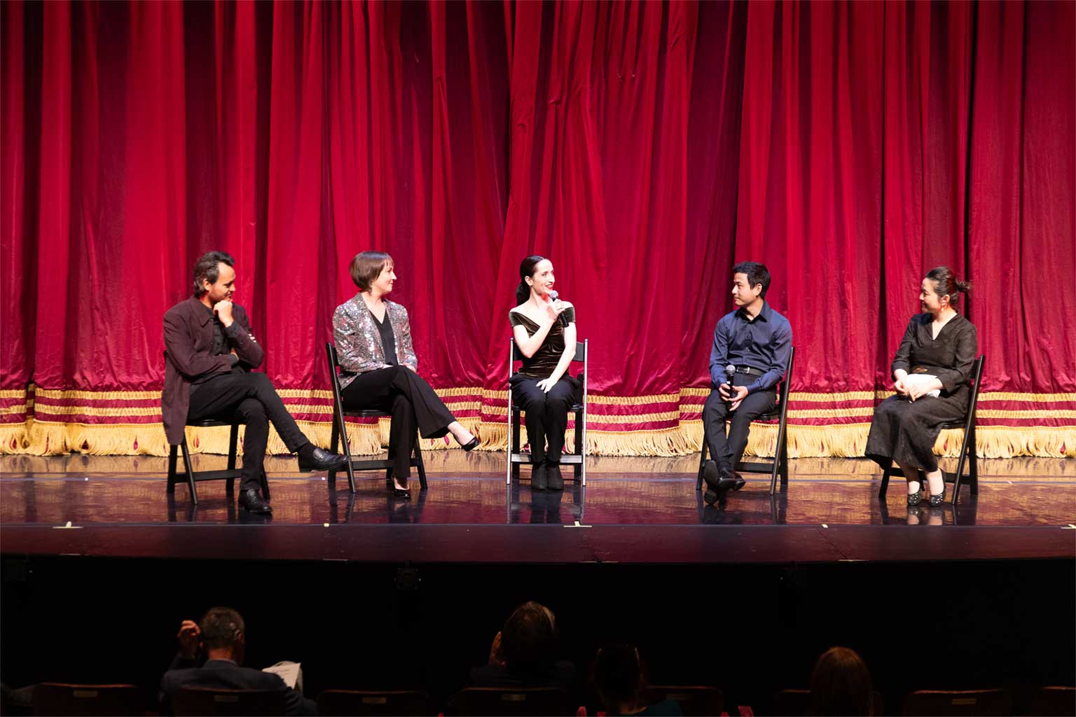 Ballet Tucson Artistic Director Margaret Mullin seated on stage with dancers and musicians, speaking to audience.