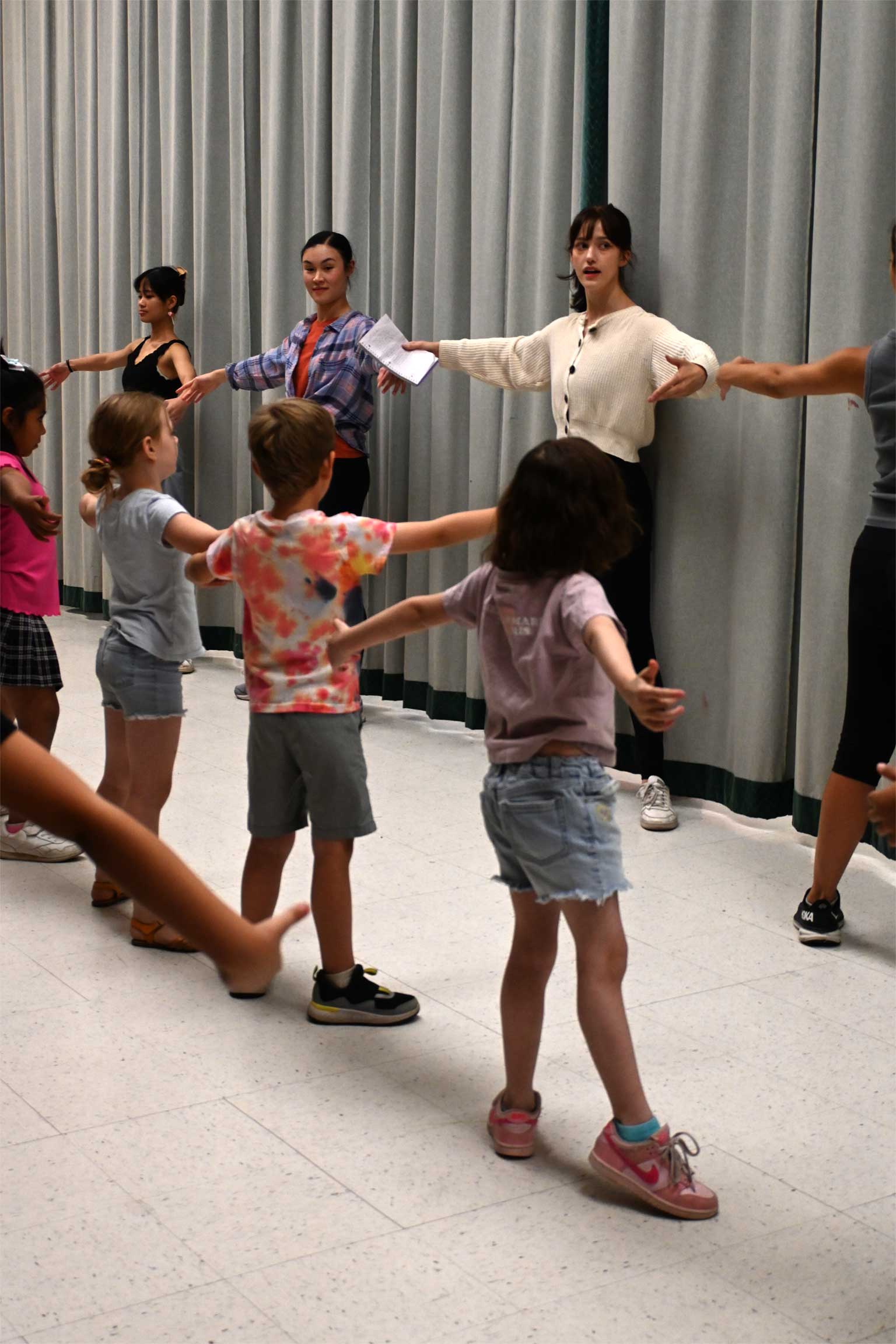 Young students sitting in a circle with their arms in the air.